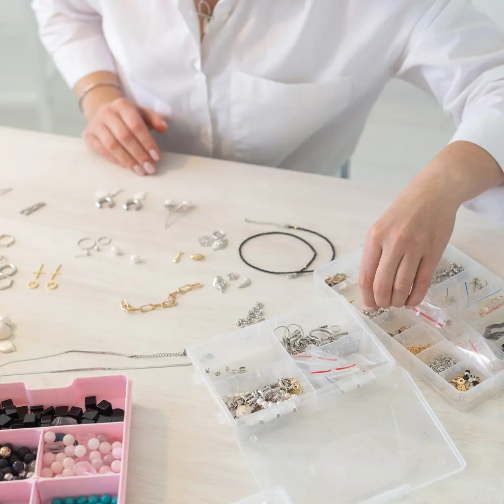 Person som lager smykker ved et bord med perler, kjeder og smykkedeler.