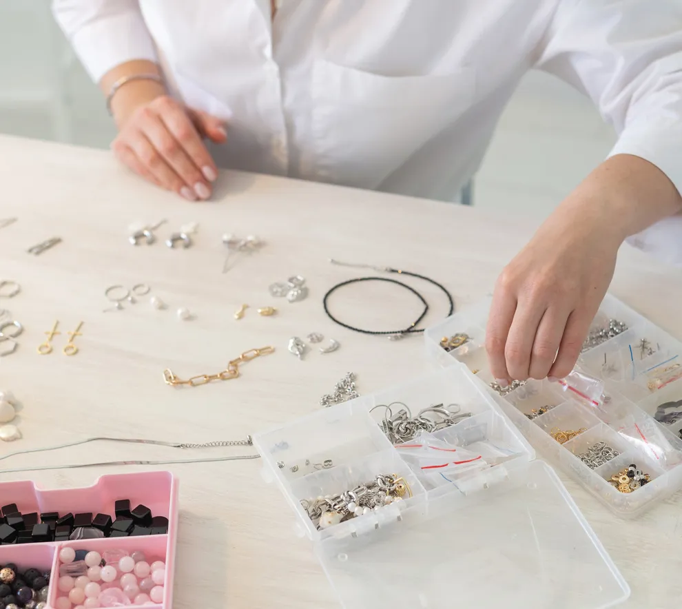 Person som lager smykker ved et bord med perler, kjeder og smykkedeler.