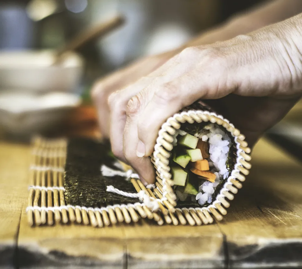 Hånd ruller fersk sushi med bambusmatte under sushikurs.