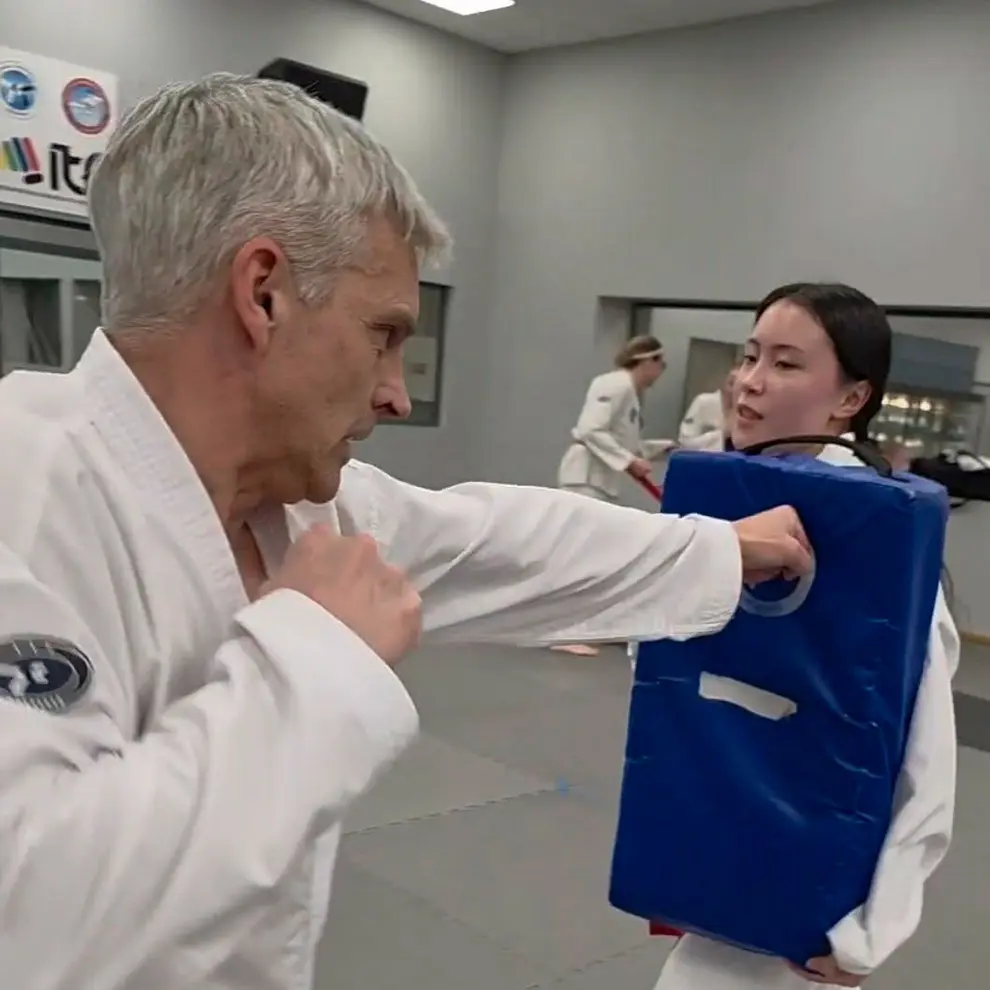 Person trener Taekwon-Do og øver slagteknikk med sparkepute i dojo