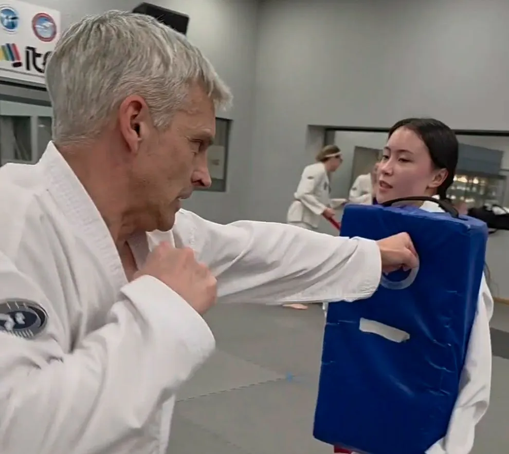 Person trener Taekwon-Do og øver slagteknikk med sparkepute i dojo