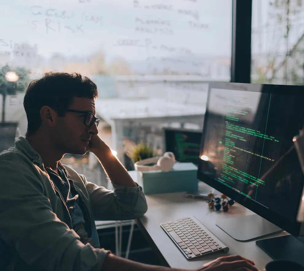 Utvikler jobber med kode på hjemmekontor foran dataskjerm med programmering i fokus.