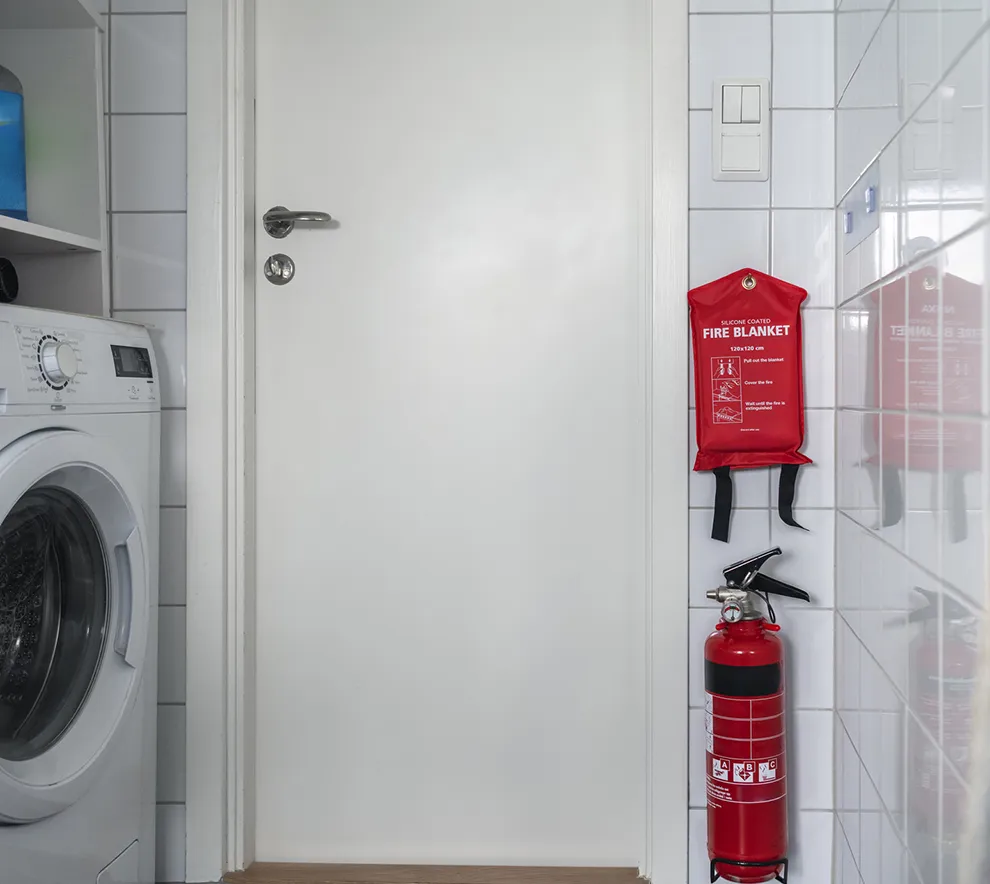 Brannslukker og brannteppe montert på vegg i et vaskerom som del av brannsikkerhet i hjemmet.
