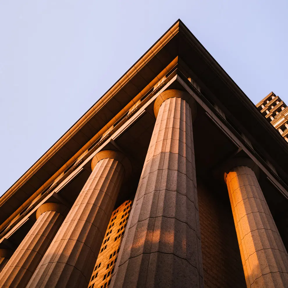 Klassisk bygning med søyler opplyst av kveldssol, symbol på jus og rettssystem.