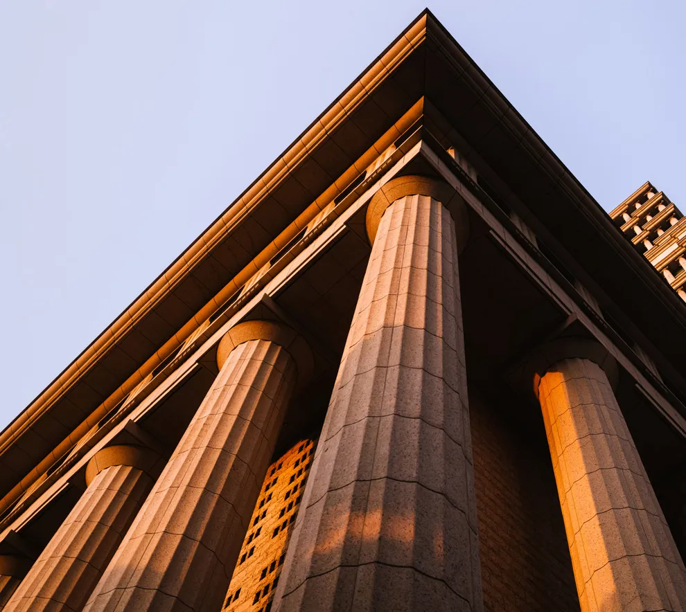 Klassisk bygning med søyler opplyst av kveldssol, symbol på jus og rettssystem.