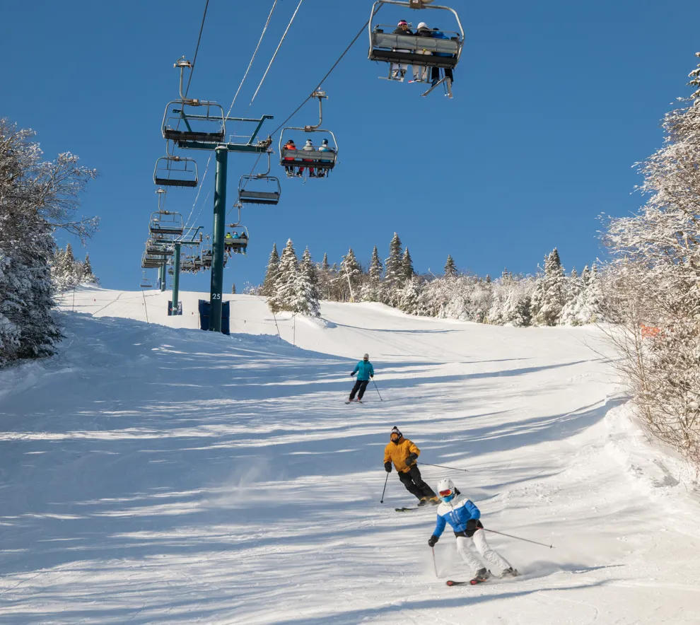 Skigåere går på ski ned alpinbakke med skiheis i bakgrunnen.