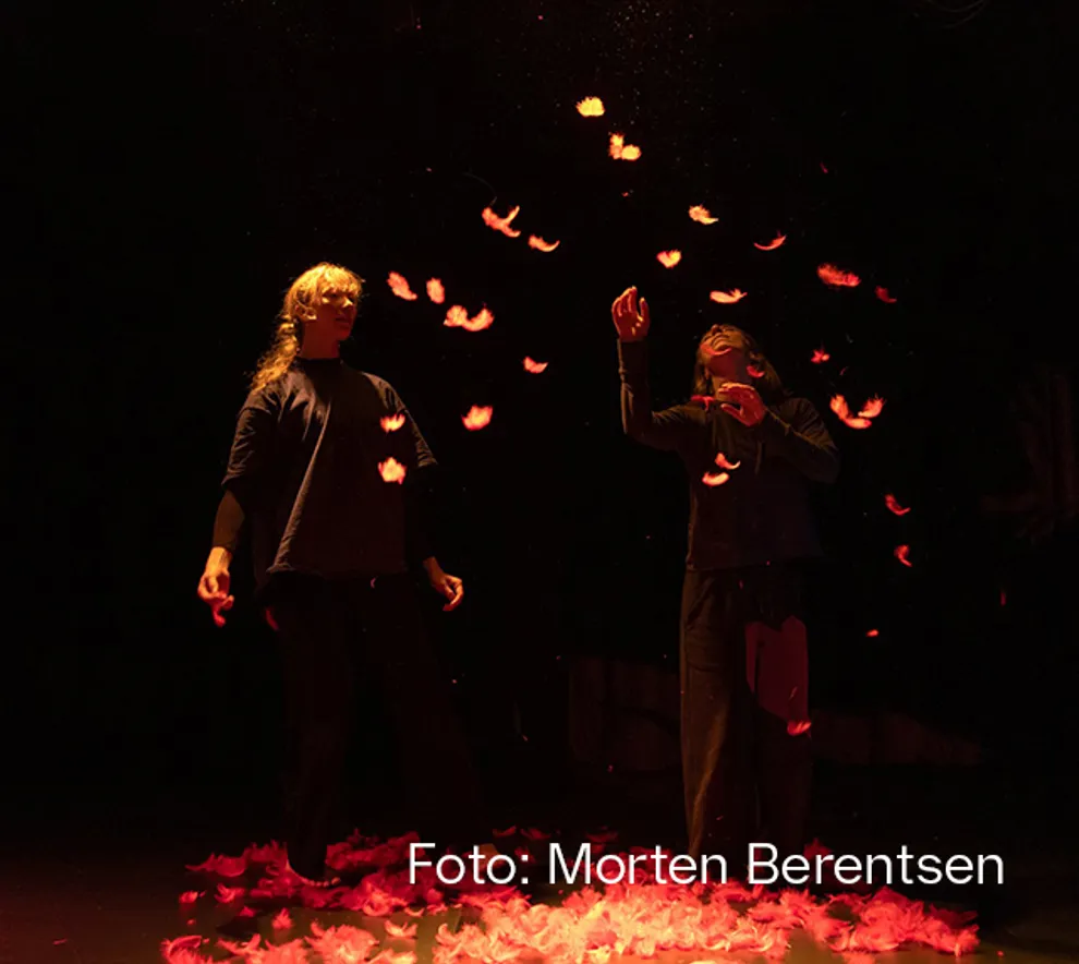 To personer på en mørklagt scene, med oransje lys på seg, fortryllet av dalende blader.