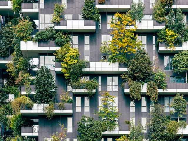 Moderne bygning med grønne balkonger dekket av trær og planter – bærekraftig arkitektur med vertikalt hagebruk.