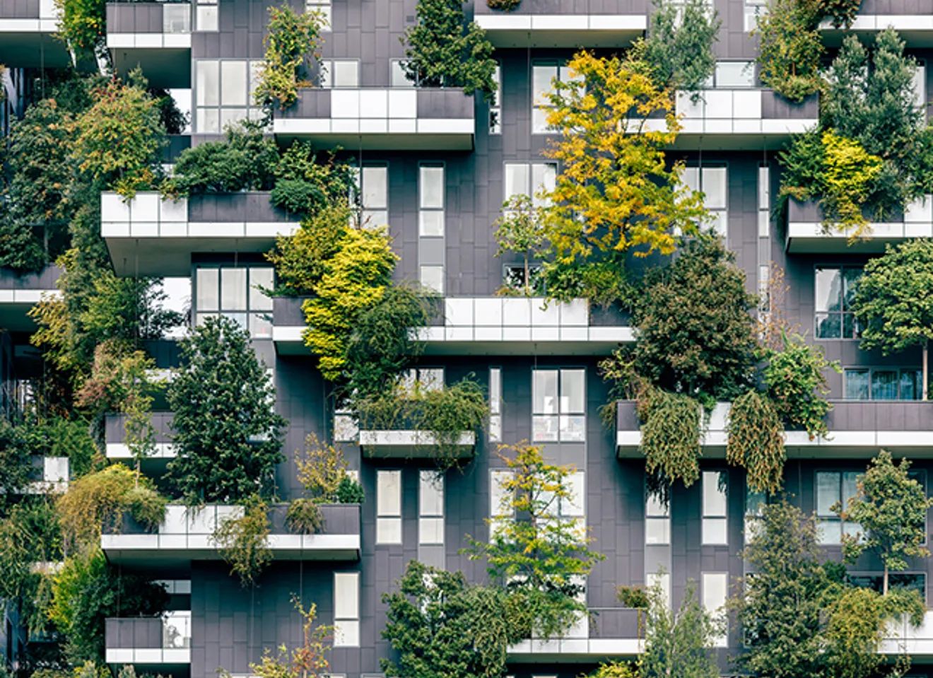 Moderne bygning med grønne balkonger dekket av trær og planter – bærekraftig arkitektur med vertikalt hagebruk.