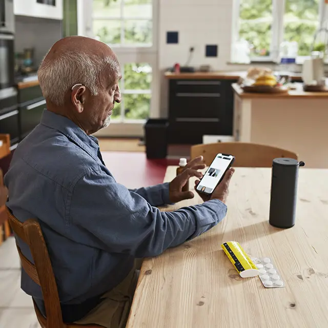 En eldre mann sitter ved kjøkkenbordet og bruker en smarttelefon.