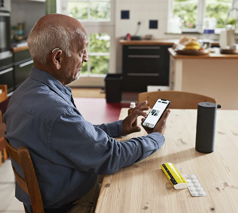 En eldre mann sitter ved kjøkkenbordet og bruker en smarttelefon.