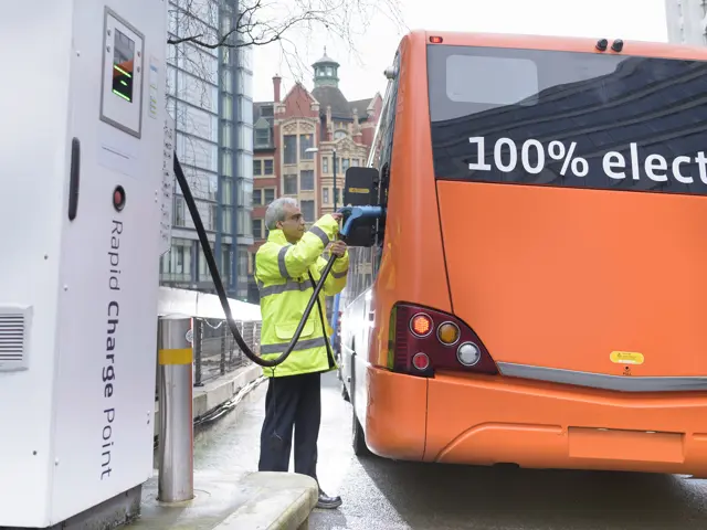 Illustrasjonsbilde av en mann i verneutstyr ved siden av en elektrisk buss med ladekabel