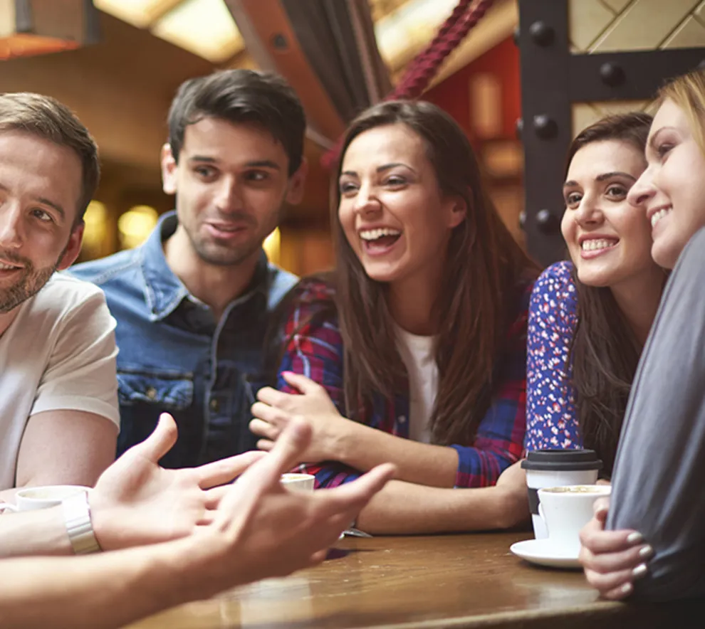 Tre kvinner og to menn rundt bord, ler smiler, ser på en tredje person som ikke er i bildet