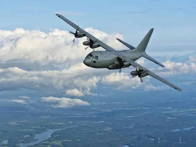 Militært transportfly over grønt landskap og skyer