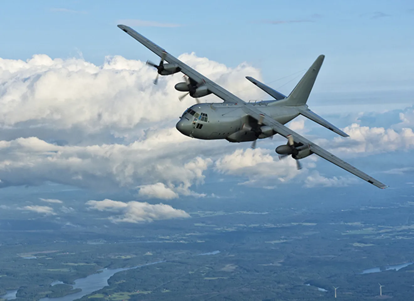 Militært transportfly over grønt landskap og skyer
