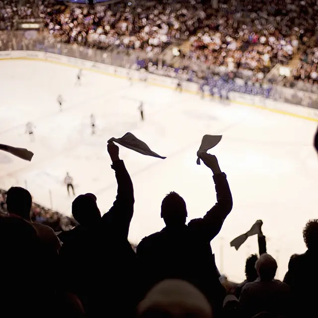 Bilde tatt fra hockey-tribunen, viser engasjerte tilskuere som står og heier, ser isen og spillerne langt ifra