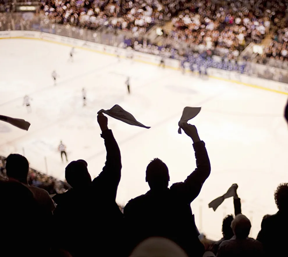 Bilde tatt fra hockey-tribunen, viser engasjerte tilskuere som står og heier, ser isen og spillerne langt ifra