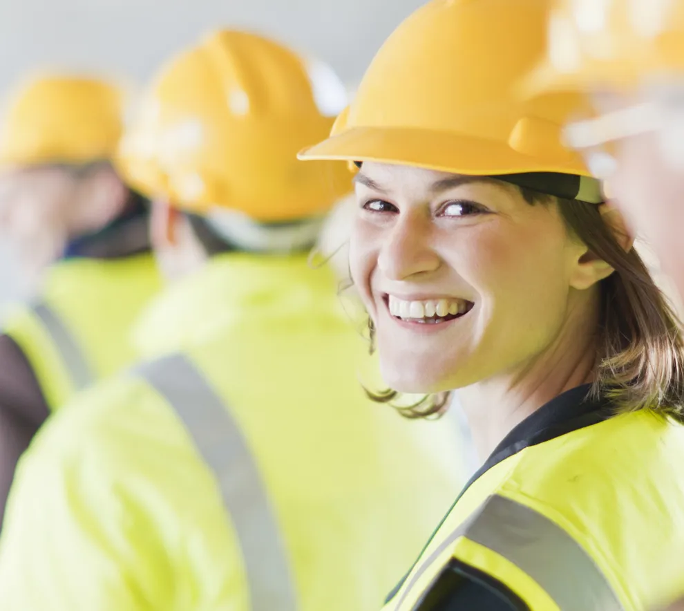 byggingeniører står på rekke med gul hjelm og kvinnen i midten snur seg og smiler mot kameraet