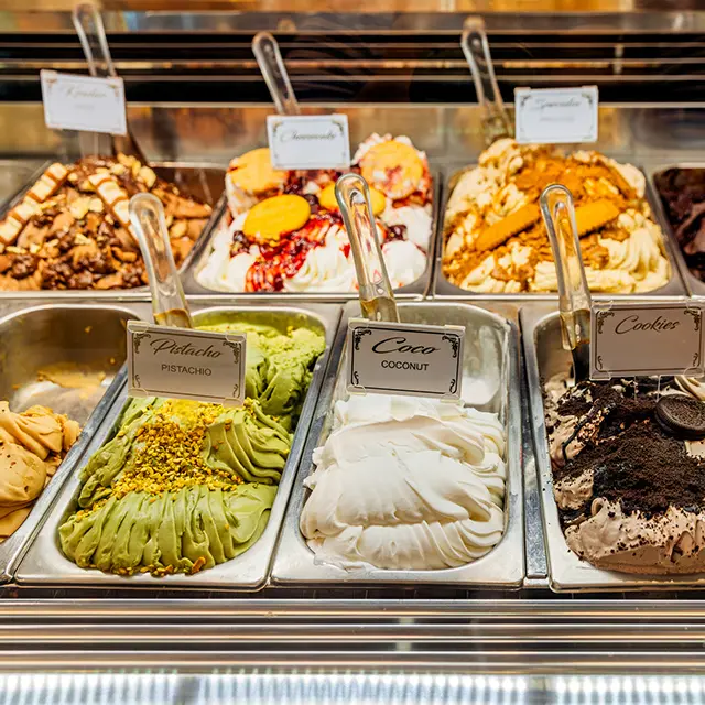 Utvalg av hjemmelaget iskrem i ulike smaker som pistasj, kokos og cookies i isdisk.