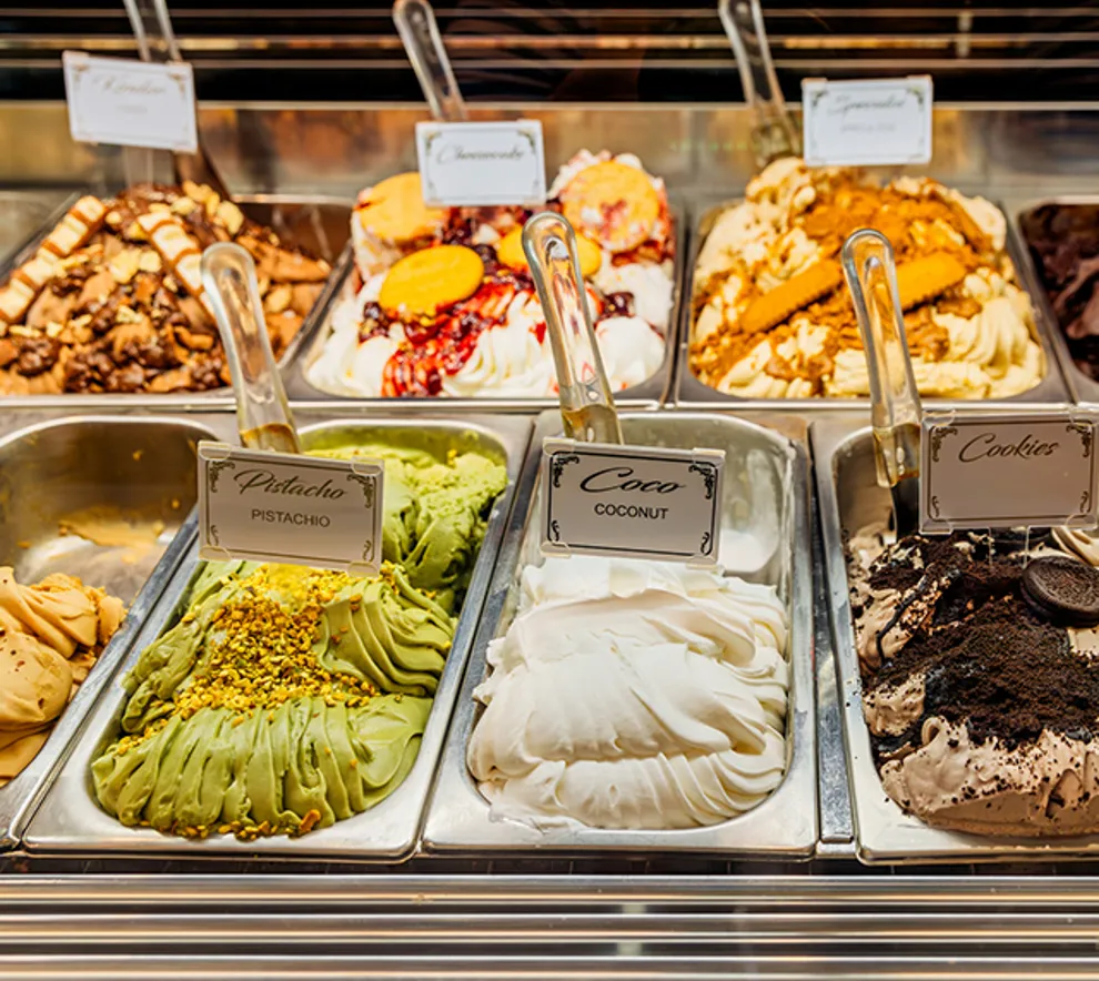 Utvalg av hjemmelaget iskrem i ulike smaker som pistasj, kokos og cookies i isdisk.