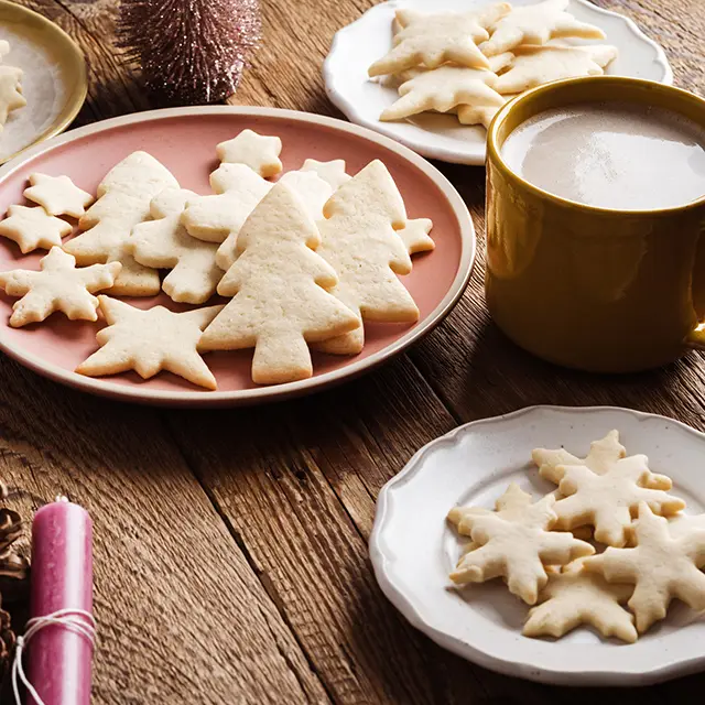 Hjemmebakte julekaker i form av stjerner og juletrær, servert med kakao på trebord.