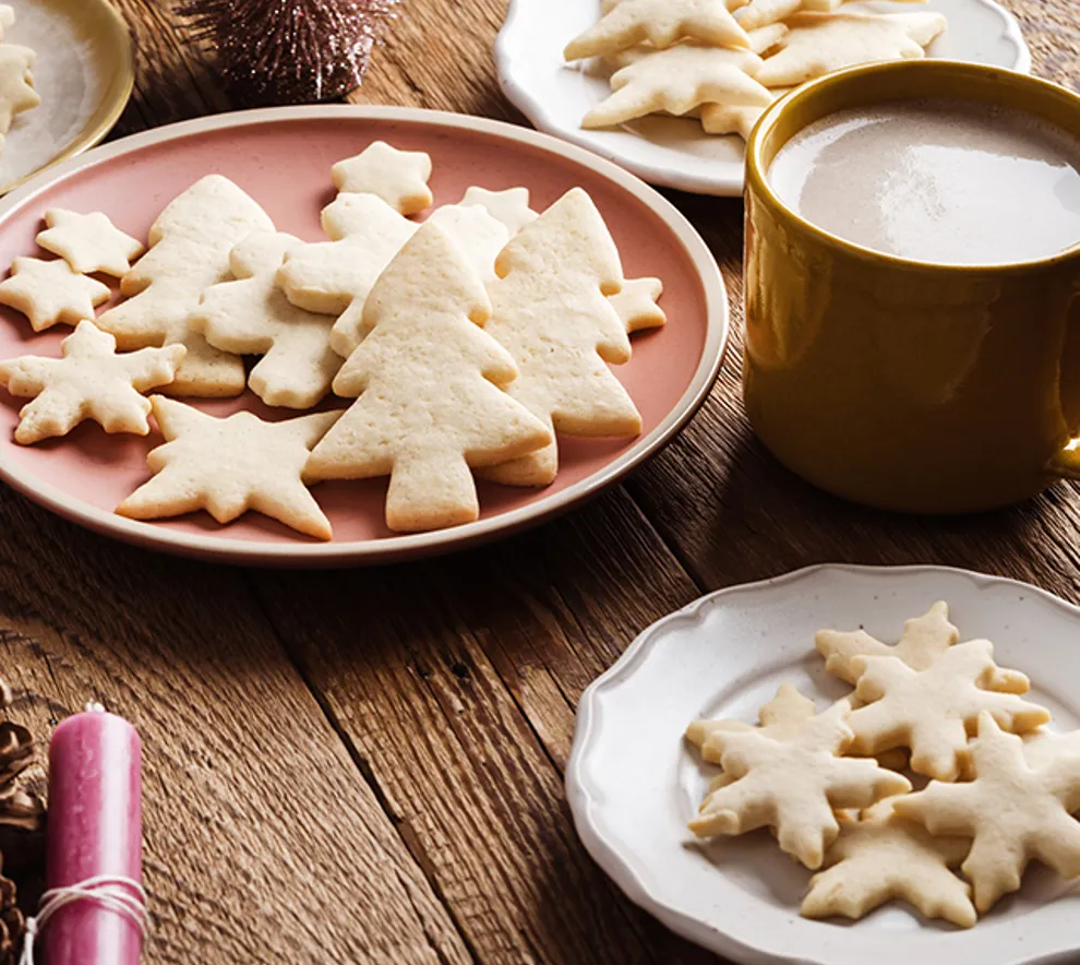 Hjemmebakte julekaker i form av stjerner og juletrær, servert med kakao på trebord.