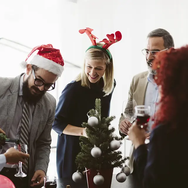 Kollegaer som feirer jul på kontoret med nisselue, reinsdyrhorn og små juletrepynt – hyggelig julebordstemning på arbeidsplassen.