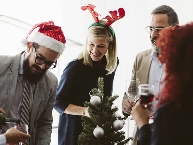 Kollegaer som feirer jul på kontoret med nisselue, reinsdyrhorn og små juletrepynt – hyggelig julebordstemning på arbeidsplassen.