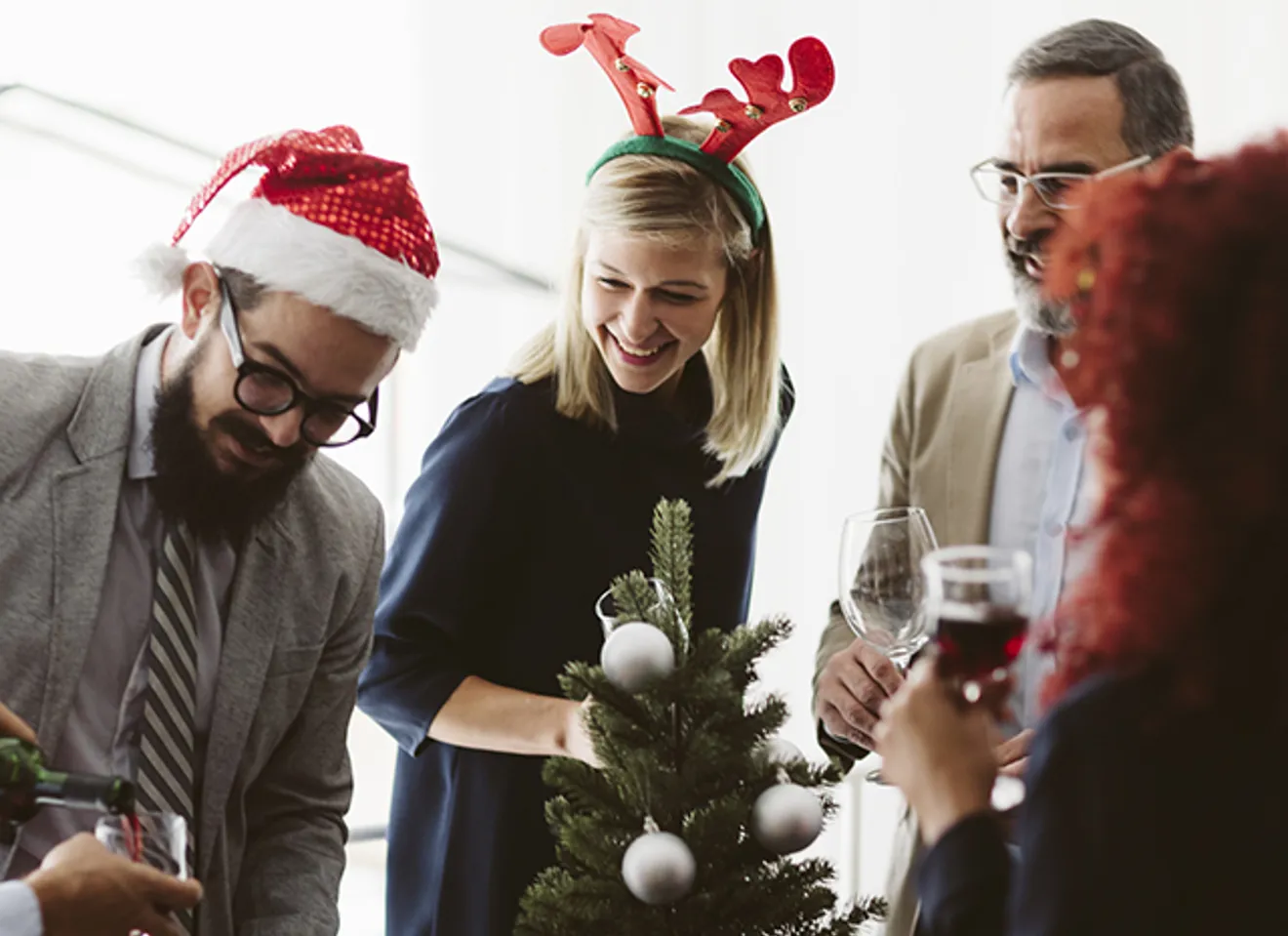 Kollegaer som feirer jul på kontoret med nisselue, reinsdyrhorn og små juletrepynt – hyggelig julebordstemning på arbeidsplassen.