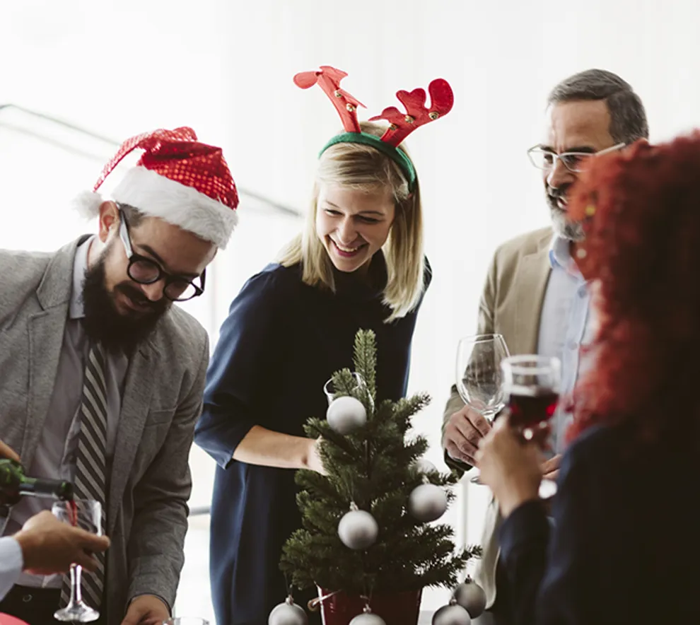 Kollegaer som feirer jul på kontoret med nisselue, reinsdyrhorn og små juletrepynt – hyggelig julebordstemning på arbeidsplassen.