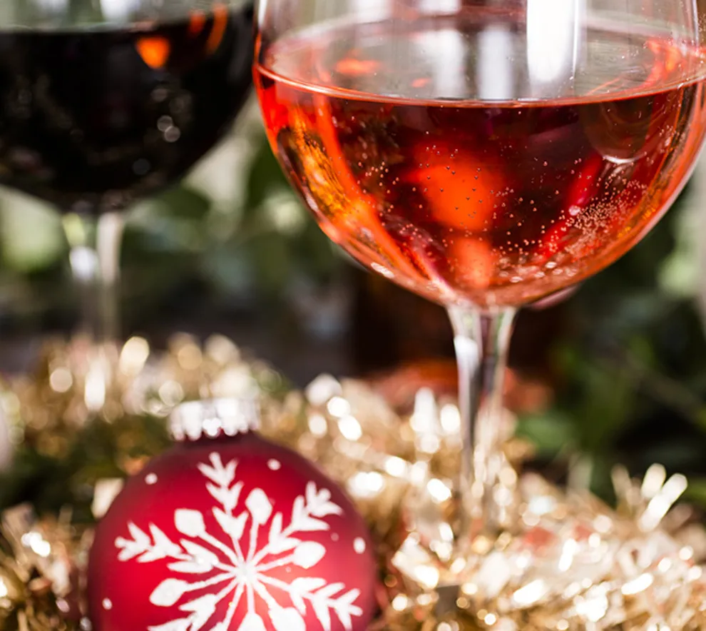Glass med rødvin og rosé omgitt av julepynt og julekule.