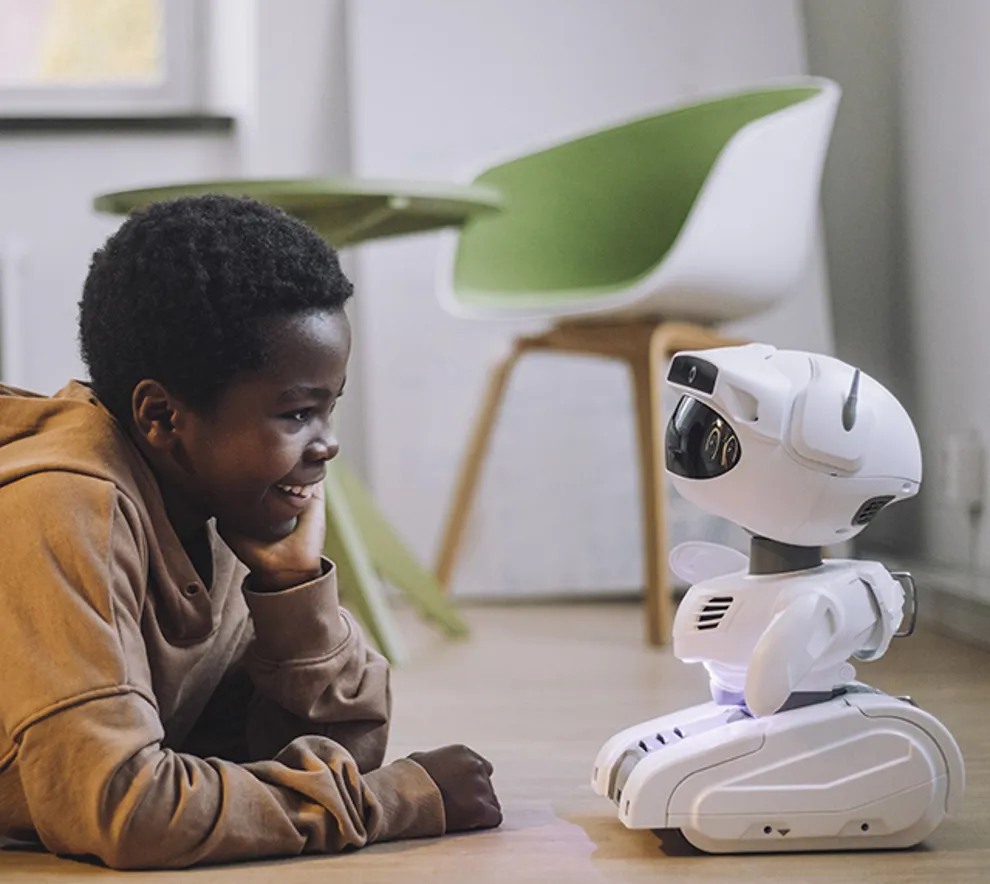 Barn ligger på gulvet og snakker med en liten, hvit futuristisk robot.