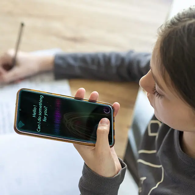 ung kvinne sitter med telefon i hånden snakker til KI, noterer samtidig