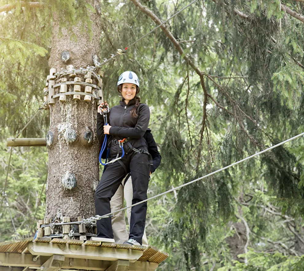 En kvinne står på en plattform foran en line blant trærne.