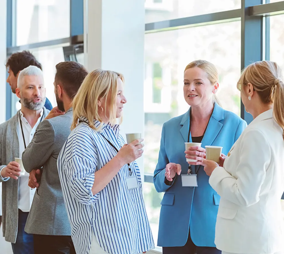 Kaffepause på konferanse, tre fornøyde kvinner i front av bildet, flere mennesker bak