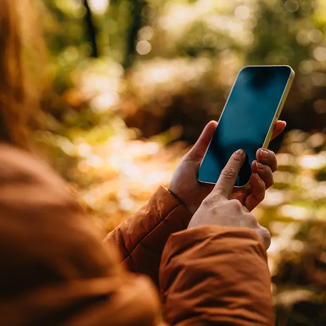 Kvinne stom står med telefon i hånden tar bilde i naturen, høstfarger