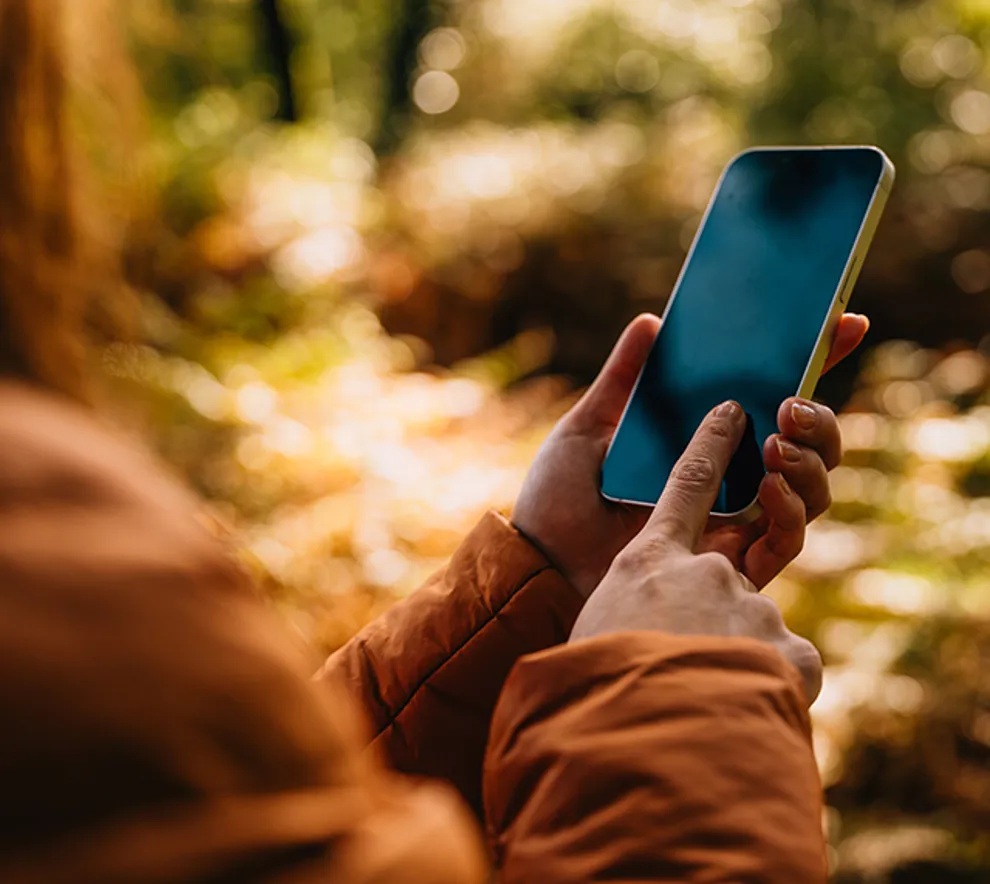 Kvinne stom står med telefon i hånden tar bilde i naturen, høstfarger