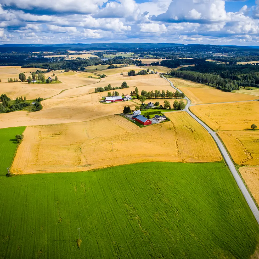 Flyfoto av gårdsbruk omgitt av jordbruksarealer og åkre i norsk landskap 