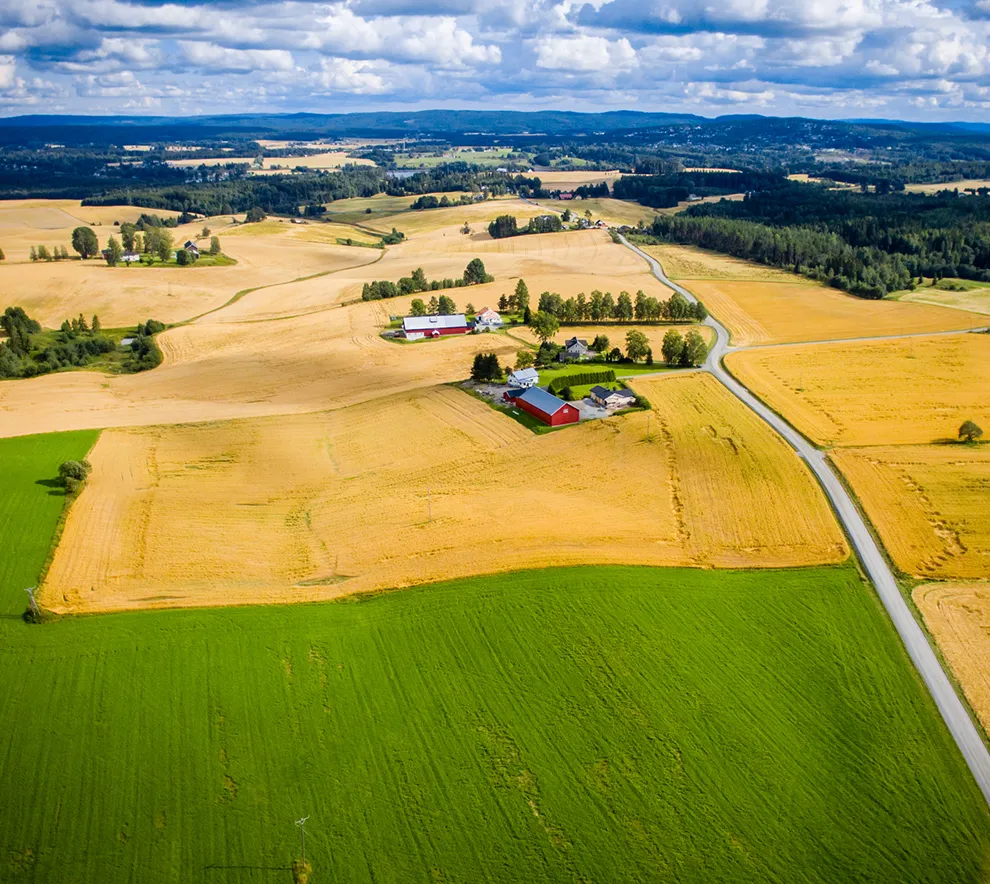 Flyfoto av gårdsbruk omgitt av jordbruksarealer og åkre i norsk landskap