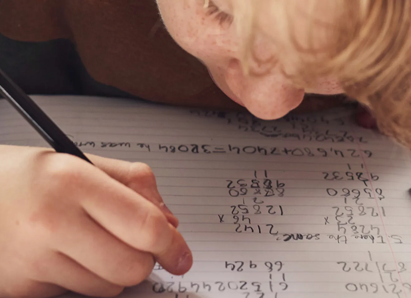 Illustrasonsbilde av et barn, en gutt, som bøyer seg over bordet for å gjøre lekser og skriver på et ark