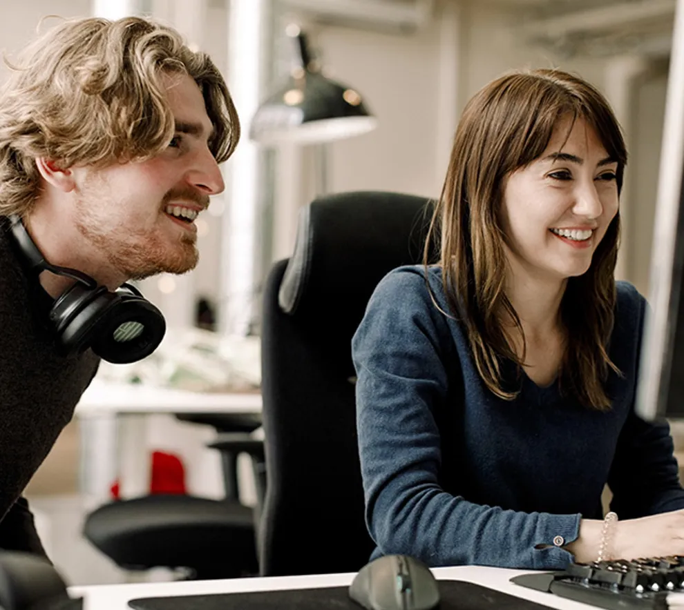 Mann og jvinne sitter ved kontorpult ser på skjerm smiler