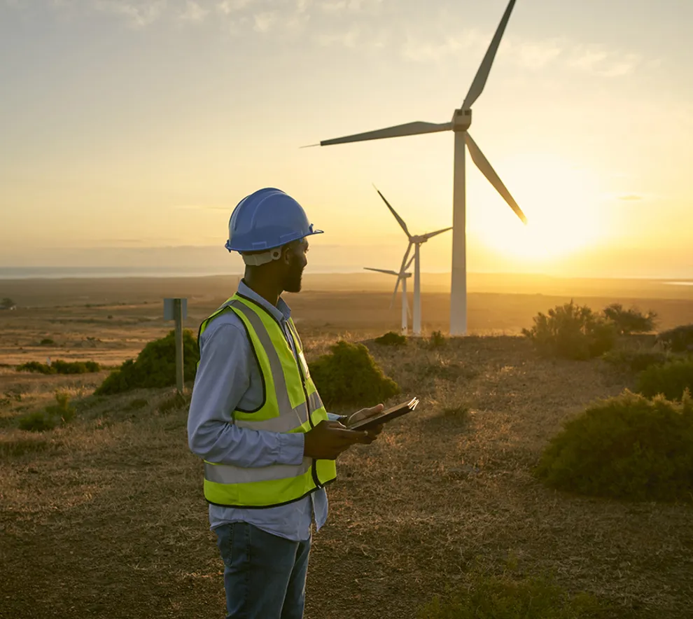 Ingeniør med nettbrett ved vindmøller i solnedgang på fornybar energiprosjekt.