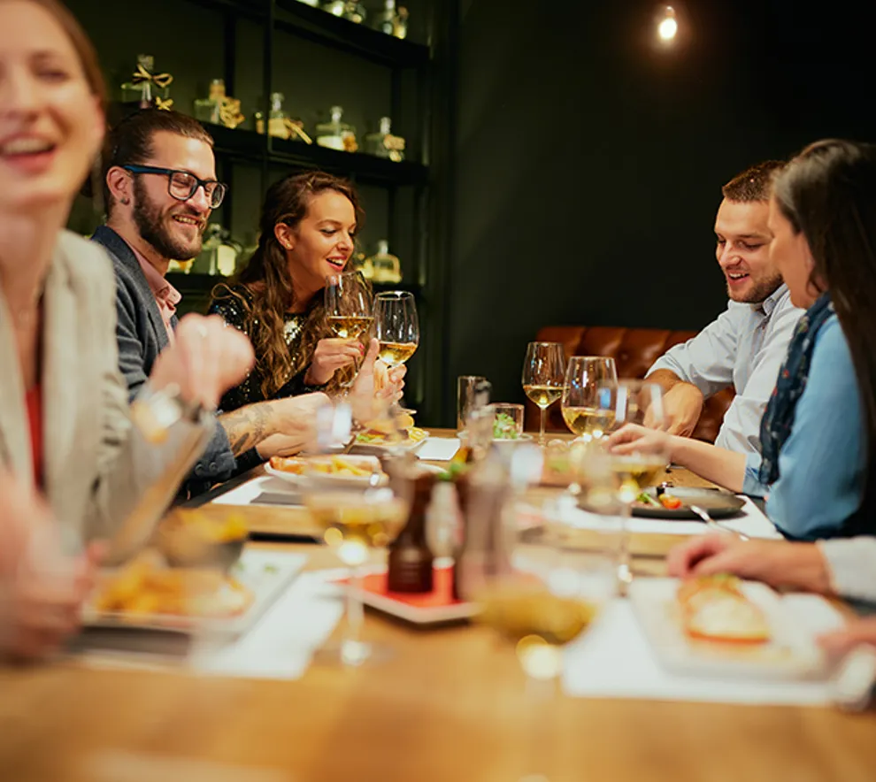 Gruppe med venner som sitter på en restaurant, spiser middag, drikker vin og har det gøy.