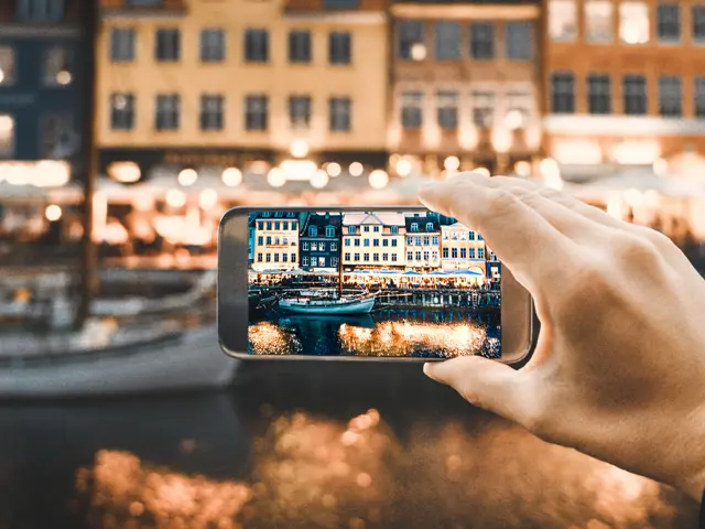 Illustrasjonsbilde av en hånd som holder en mobil og ta bilde av en by om natten