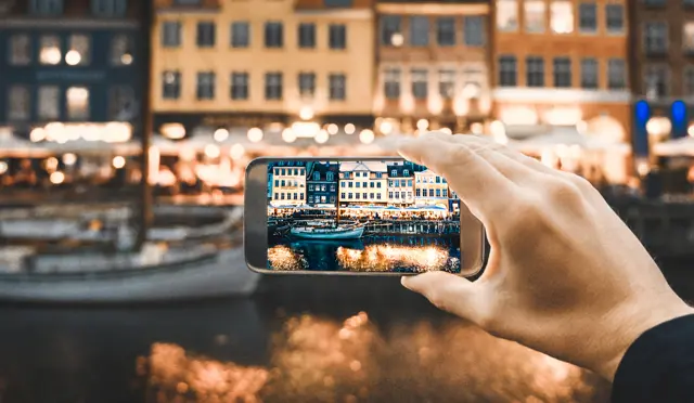 Illustrasjonsbilde av en hånd som holder en mobil og ta bilde av en by om natten