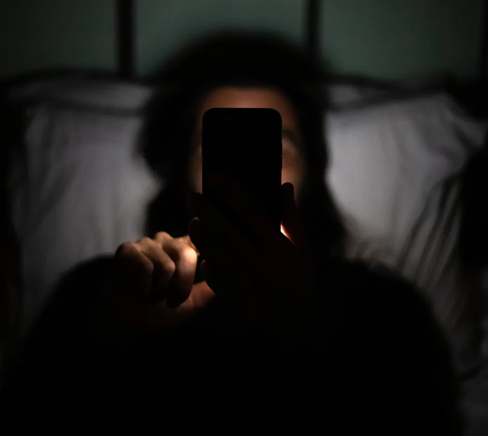 Person bruker mobiltelefon i mørket med skjermen som eneste lys.