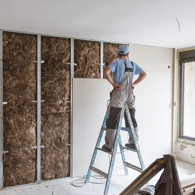 Håndverker monterer gipsplater over lydisolasjon i bolig under oppussing.