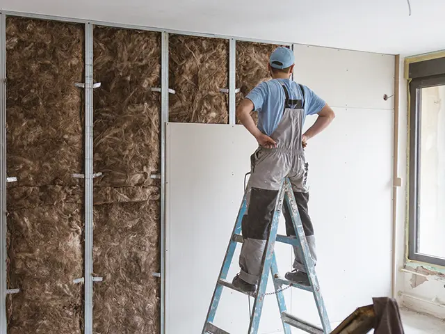 Håndverker monterer gipsplater over lydisolasjon i bolig under oppussing.
