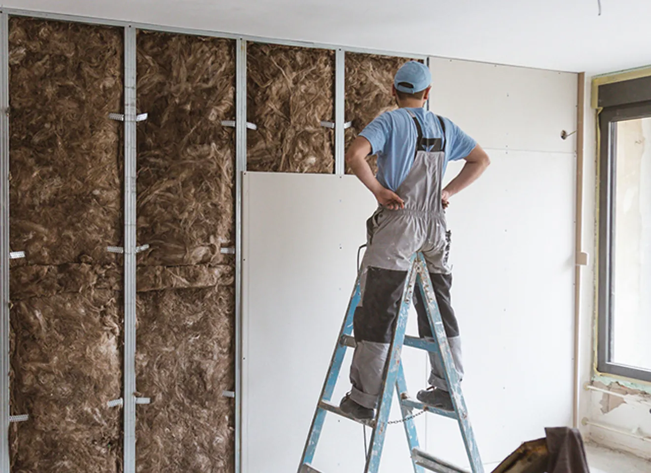 Håndverker monterer gipsplater over lydisolasjon i bolig under oppussing.