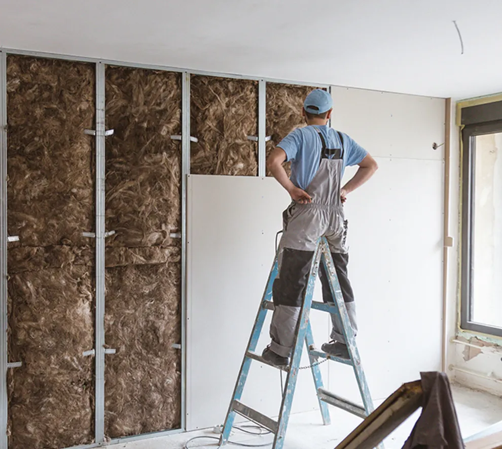 Håndverker monterer gipsplater over lydisolasjon i bolig under oppussing.